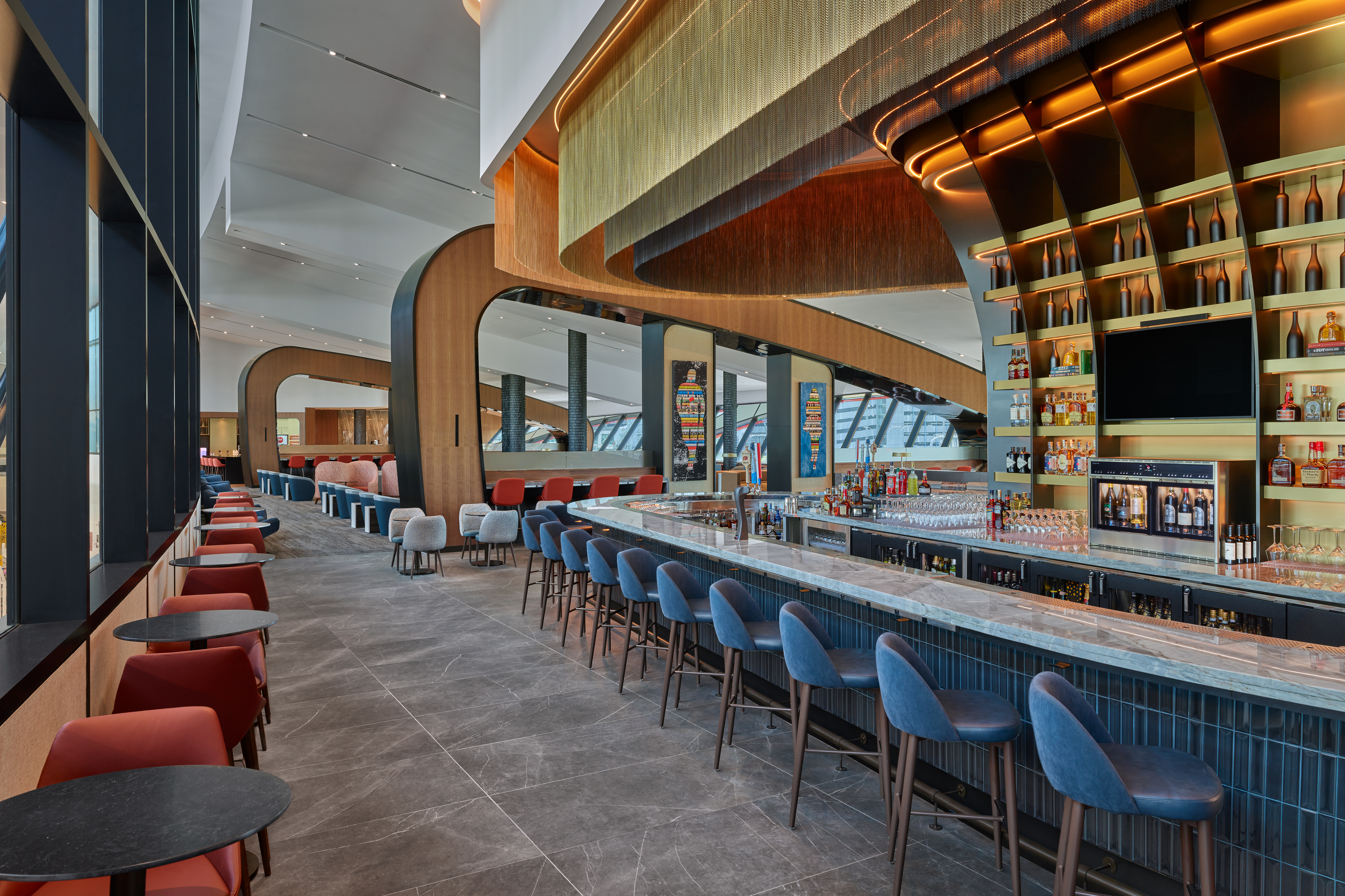 Perhaps the most eye-catching element of Delta's newest Sky Club at Boston-Logan Airport is the premium bar, which features a layered, champagne-toned mesh ceiling overhang and a dramatic backlit beverage display. 
