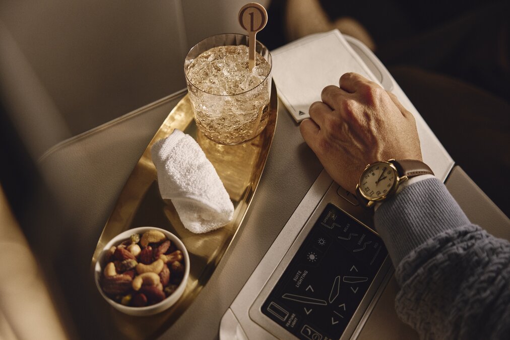 Passenger enjoys a welcome beverage and mixed nuts beside Delta One seat controls.