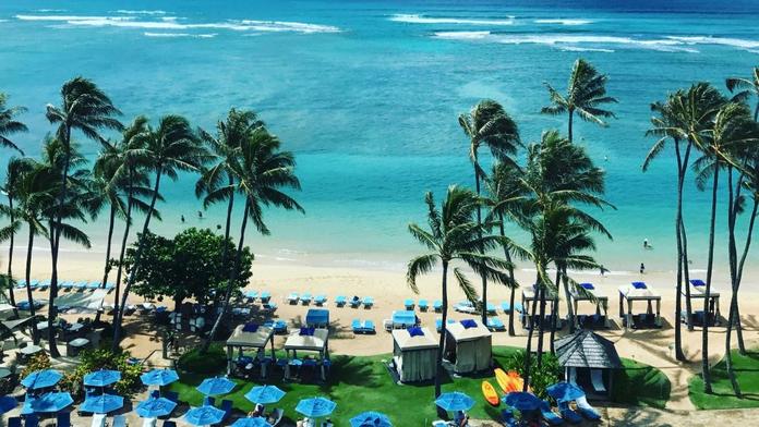 An overhead shot of a beach in Honolulu, Hawaii with umbrellas and palm trees