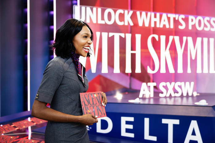 Austin-based Delta Air Lines flight attendant cheerfully welcomes visitors to SXSW 2024 at Austin-Bergstrom International Airport, with an invitation to grab a copy of Delta's curated guide to navigating SXSW 2024.