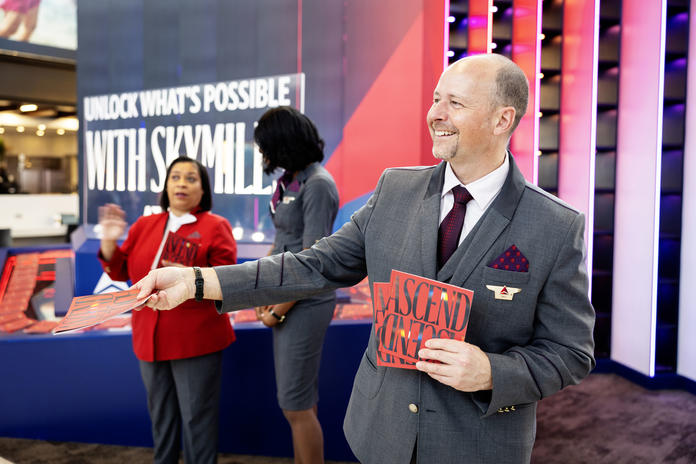 Austin-based Delta Air Lines flight attendant cheerfully welcomes visitors to SXSW 2024 at Austin-Bergstrom International Airport, with an invitation to grab a copy of Delta's curated guide to navigating SXSW 2024.