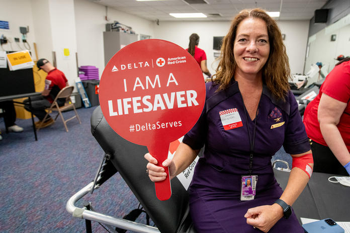 A Delta employee holds up a sign that says "I am a lifesaver" while giving blood.