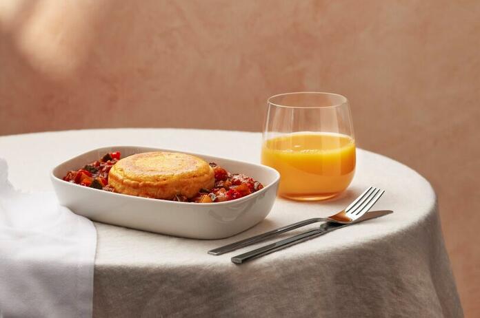 Plated spanish tortilla dish displayed on table with white cloth and silverware, glass of orange juice to the right.