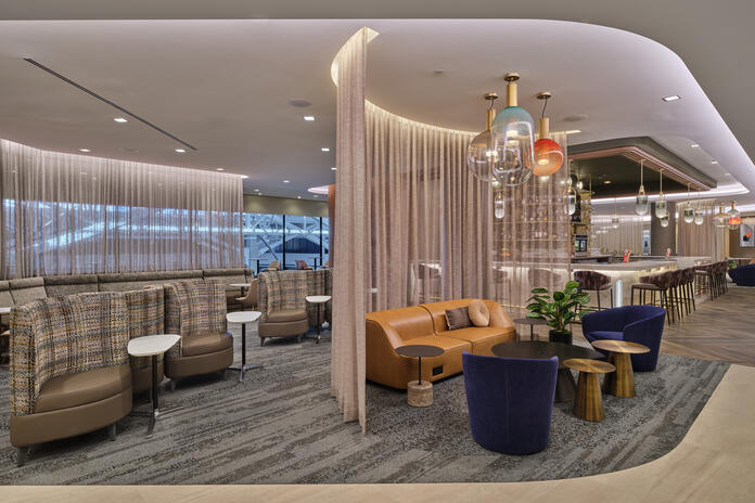 West lounge area with curved seating, soft lighting, privacy curtains and a bar with colorful hanging lights