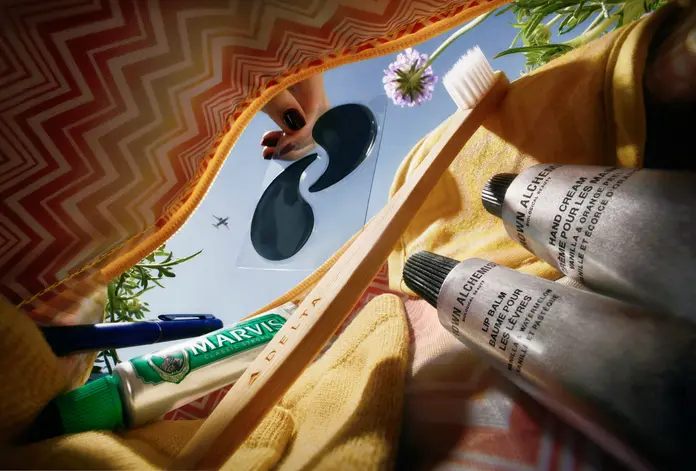 View inside a Missoni amenity kit showing a toothbrush, toothpaste, lip balm, hand cream, eye mask, and pen against a blue sky.