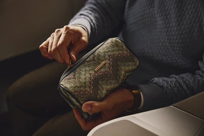 Hands opening a patterned travel amenity kit while seated in a premium airline cabin.
