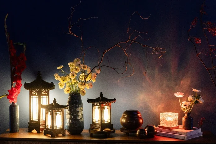 Decorative lanterns, flowers and accent lighting arranged on a table against a dark blue backdrop.