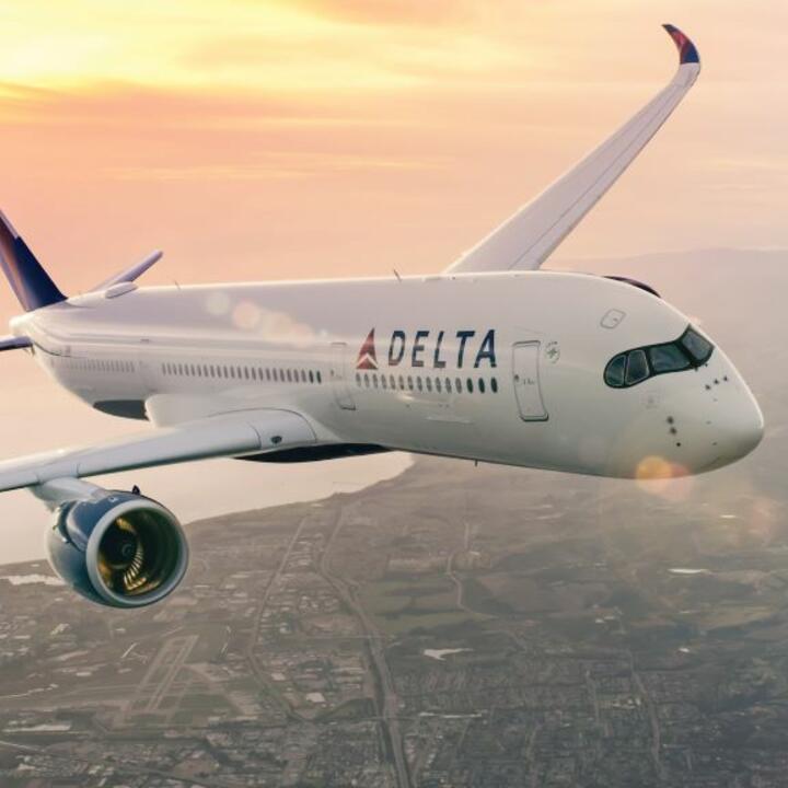 Delta aircraft flying above a coastal city with sun setting in background