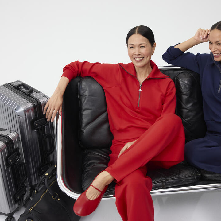 Two smiling women, sitting next to each other dressed in red and navy Spanx outfits.