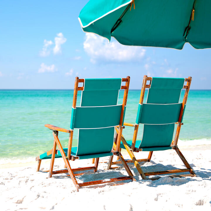 Two empty beach chairs in the sand facing turquoise blue ocean.