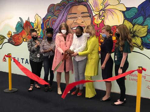 Wellspring and Delta leaders and employees cut a ribbon to present the final mural that symbolizes Delta's mission to combat human trafficking. The mural is of a smiling woman with flowers and rainbows behind her head. Beneath the image is the word 'free' and an imagery for Delta and Wellspring's partnership.