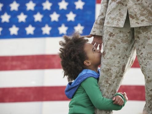 A child hugs a service member in uniform.