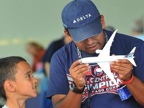 Man holds model airplane while boy looks on.