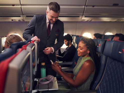 A Delta Flight Attendant assists a customer seated in Delta Comfort+ with their mobile device.