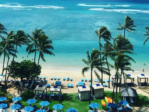 An overhead shot of a beach in Honolulu, Hawaii with umbrellas and palm trees