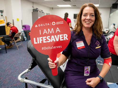 A Delta employee holds up a sign that says "I am a lifesaver" while giving blood.