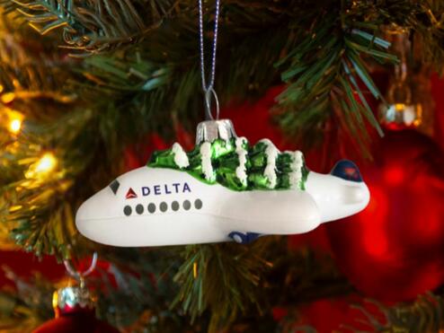 Soar into style with our Festive Delta Plane Ornament. Made of glass with a whimsical tree on top, make sure to snag one before it takes off! 