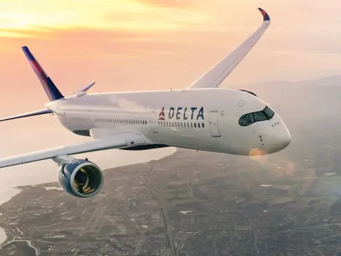 Delta aircraft flying above a coastal city with sun setting in background