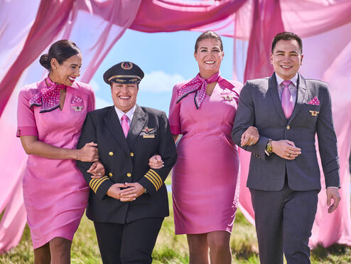 Four Delta employees in pink uniforms walking arm in arm
