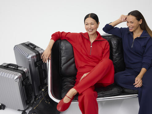 Two smiling women, sitting next to each other dressed in red and navy Spanx outfits.