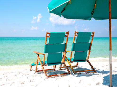 Two empty beach chairs in the sand facing turquoise blue ocean.