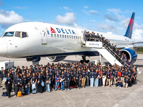 Group shot of DREAM flight attendees standing in front of Delta plane on tarmac. 