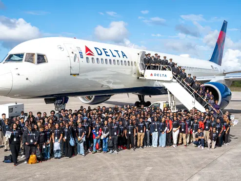 Group shot of DREAM flight attendees standing in front of Delta plane on tarmac. 
