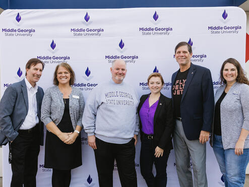 Six people standing in front of a Middle Georgia State University step-and-repeat banner, posing for a group photo.
