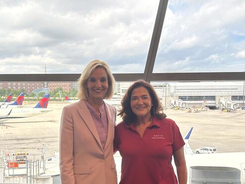 Delta employees Allison Ausband and Nancy Cohn posing against a backdrop of the Boston airport ramp.