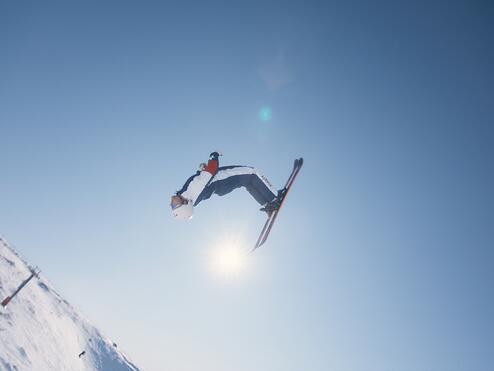 A skier performs a high aerial trick against a clear blue sky on a snowy mountain slope