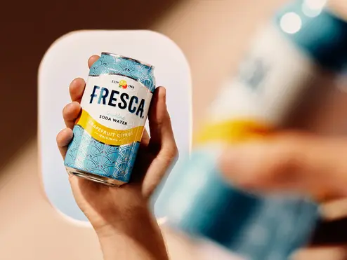 Hand holding a chilled Fresca grapefruit citrus soda can, with an airplane window softly blurred in the background.