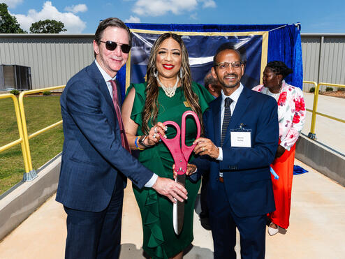 Group of individuals holding oversized ceremonial scissors at an outdoor ribbon-cutting event.