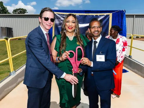 Group of individuals holding oversized ceremonial scissors at an outdoor ribbon-cutting event.