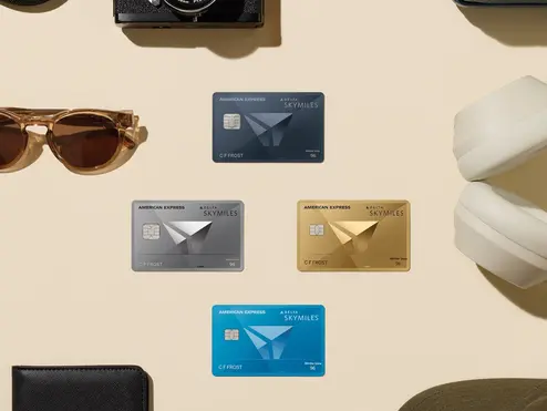 Flat lay of Delta SkyMiles American Express Cards surrounded by travel essentials, including a passport, camera, sunglasses, headphones, and luggage accessories.