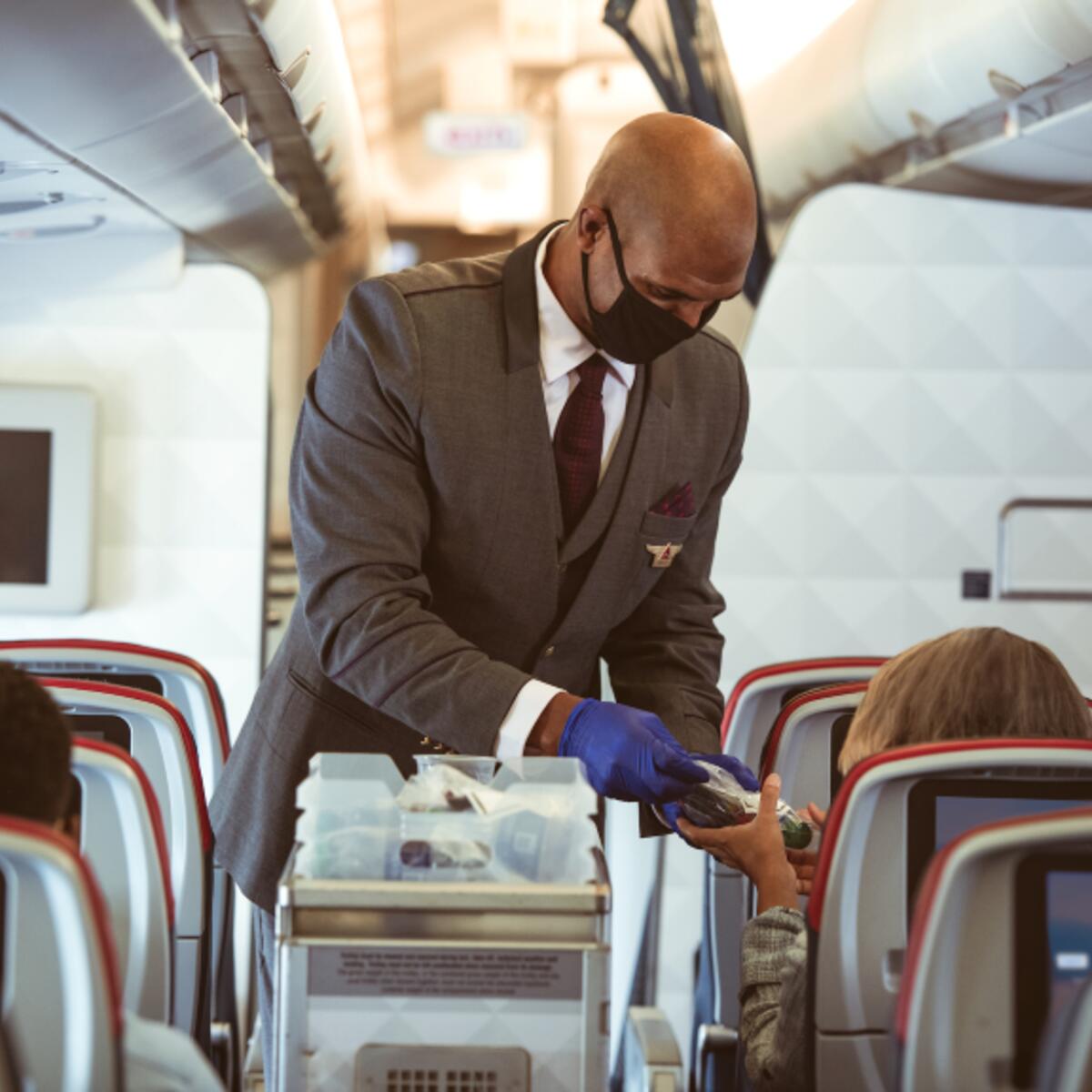 A masked flight attendant serves customers.
