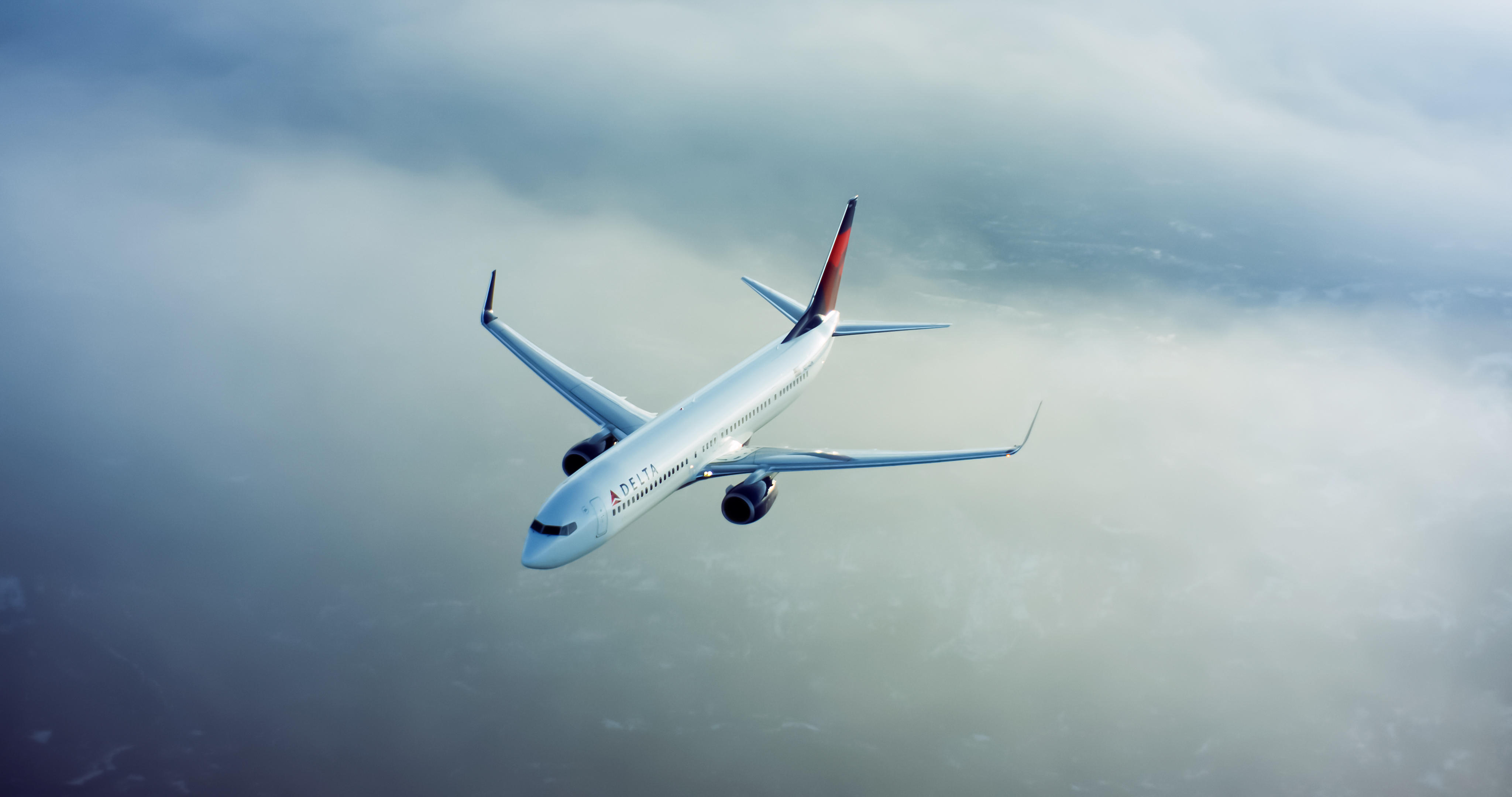 A 737-900 flies through clouds with a cityscape underneath.