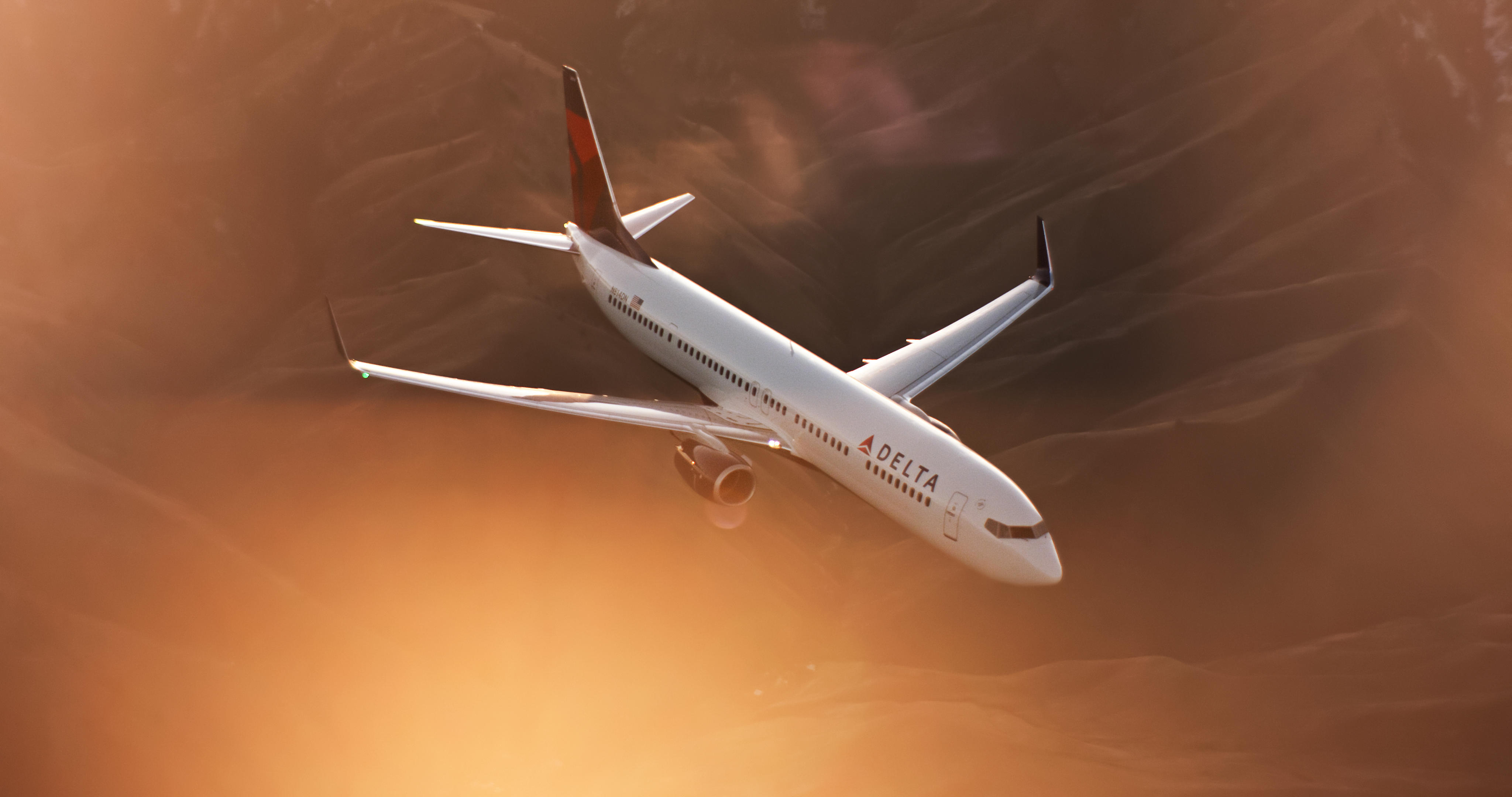 A 737-900 flies while a mountainous terrain displays in the distance.