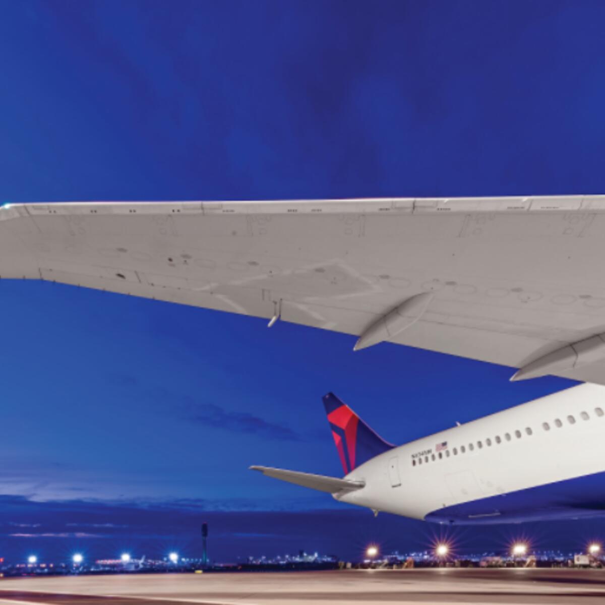 Overlooking an evening skyline lit by the runway, Delta's Boeing 767-400 dorsal area features a wingspan of 171 feet and a tail height of over 50 inches.