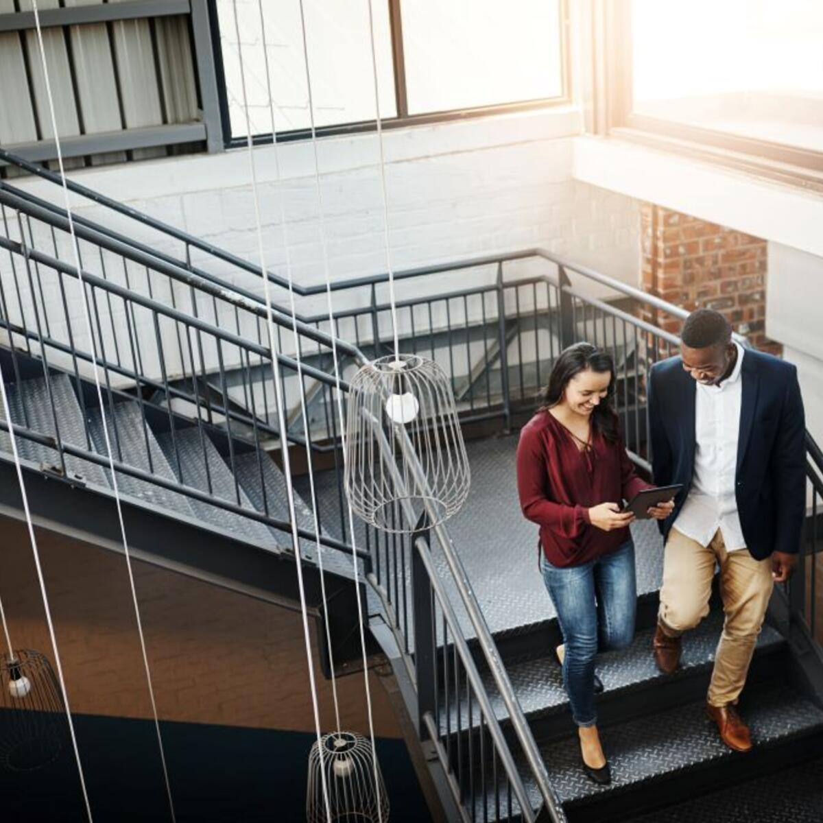Two people walking down a flight of stairs looking at a tablet.