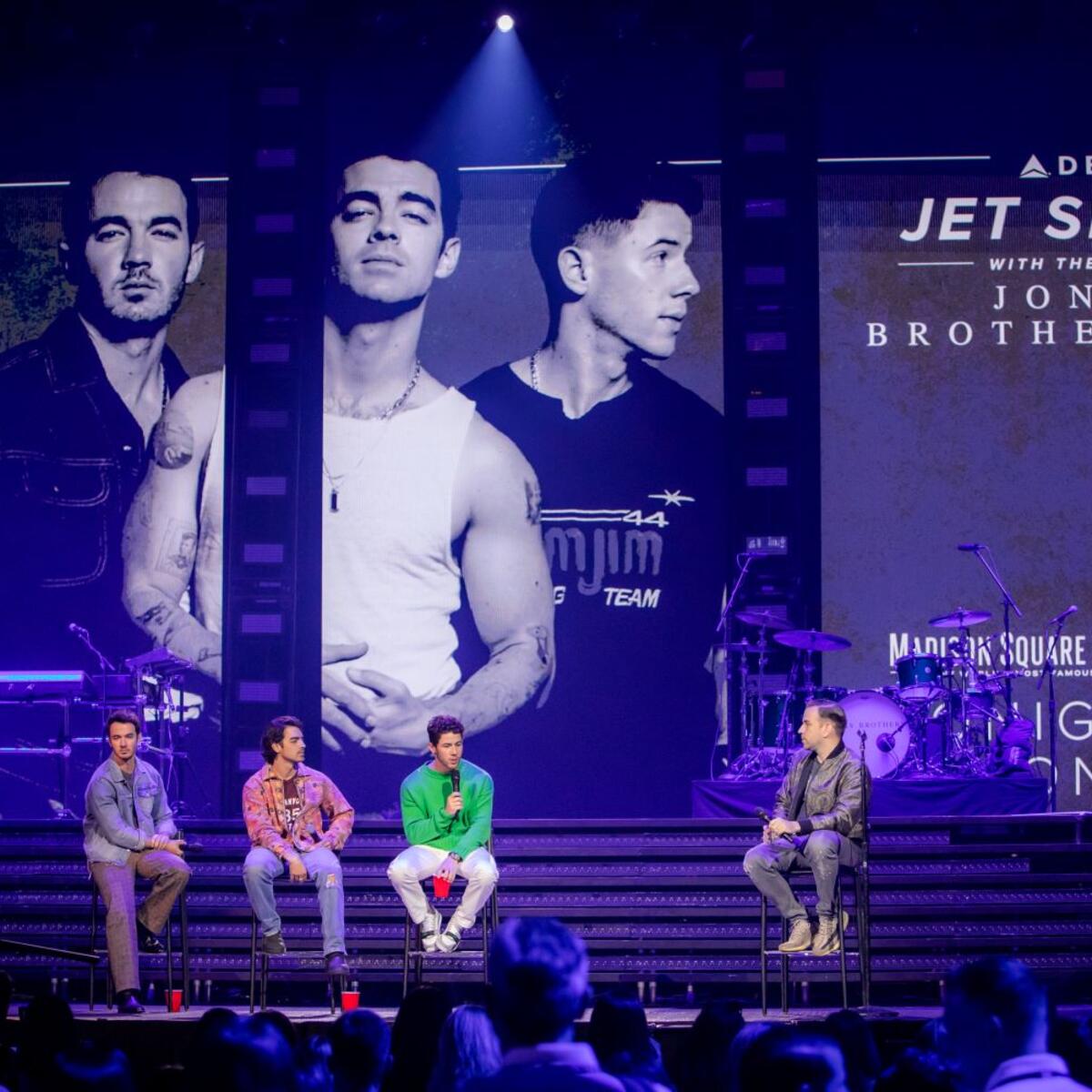 Jonas Brothers interviewing on stage with Delta-sponsored sign in background.