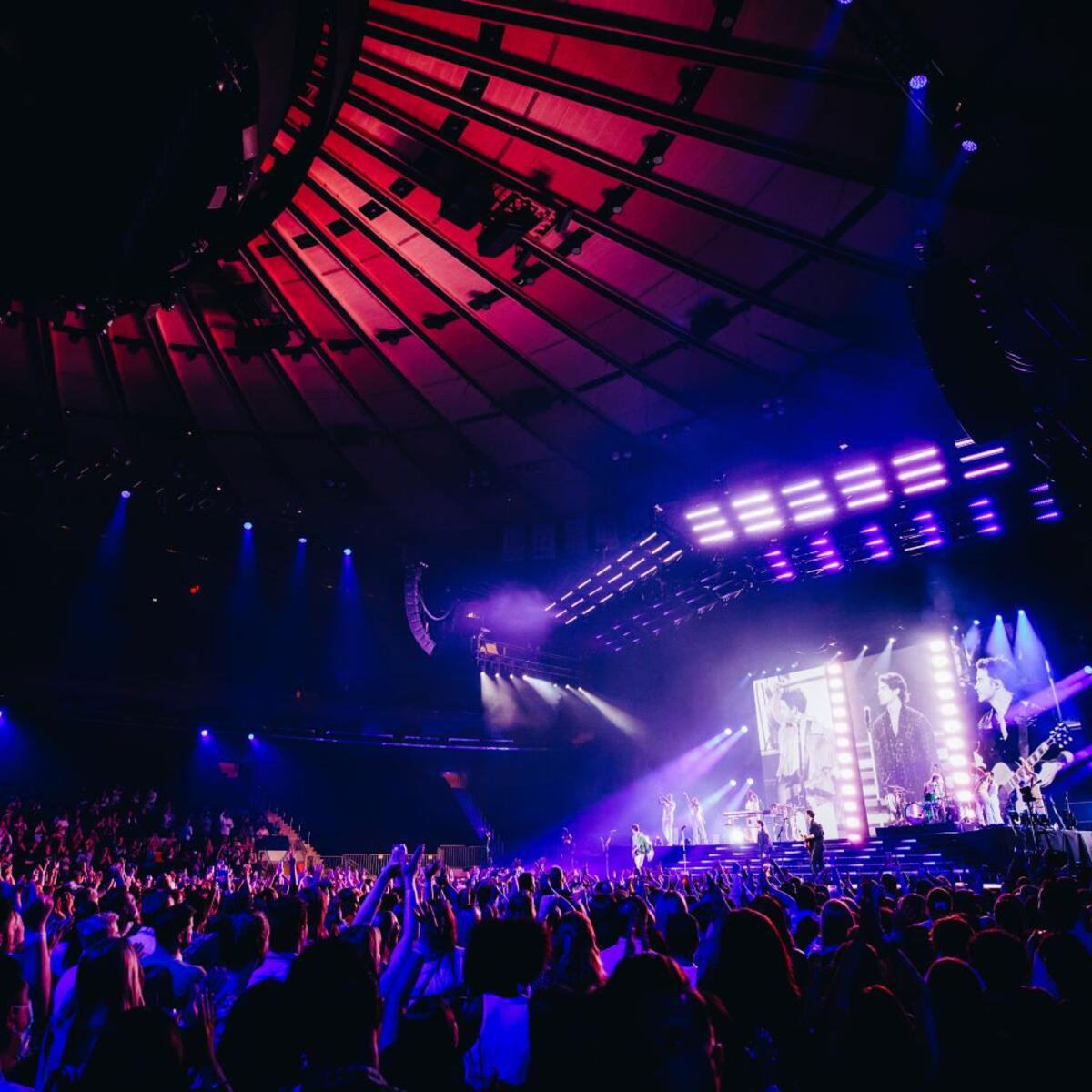 Jonas Brothers concert with full crowd in stadium and bright lights on the stage.