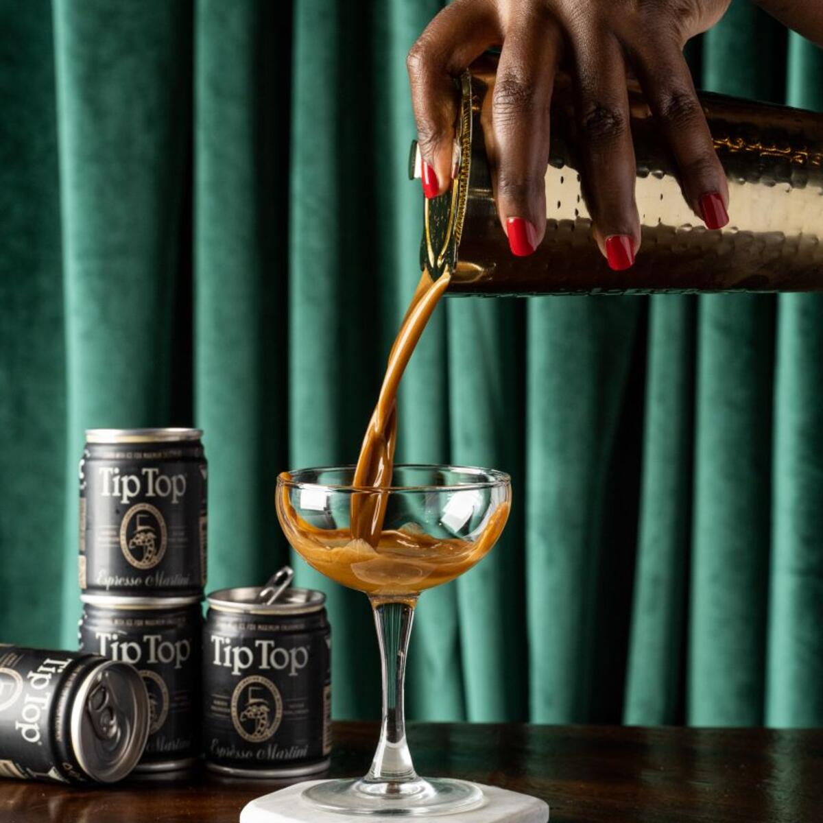 A hand pouring Tip Top Proper Cocktails' Espresso Martini into a martini glass.