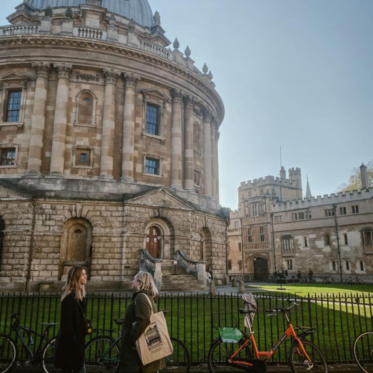Two people stand in front of the Radcliffe Camera building at the University of Oxford.