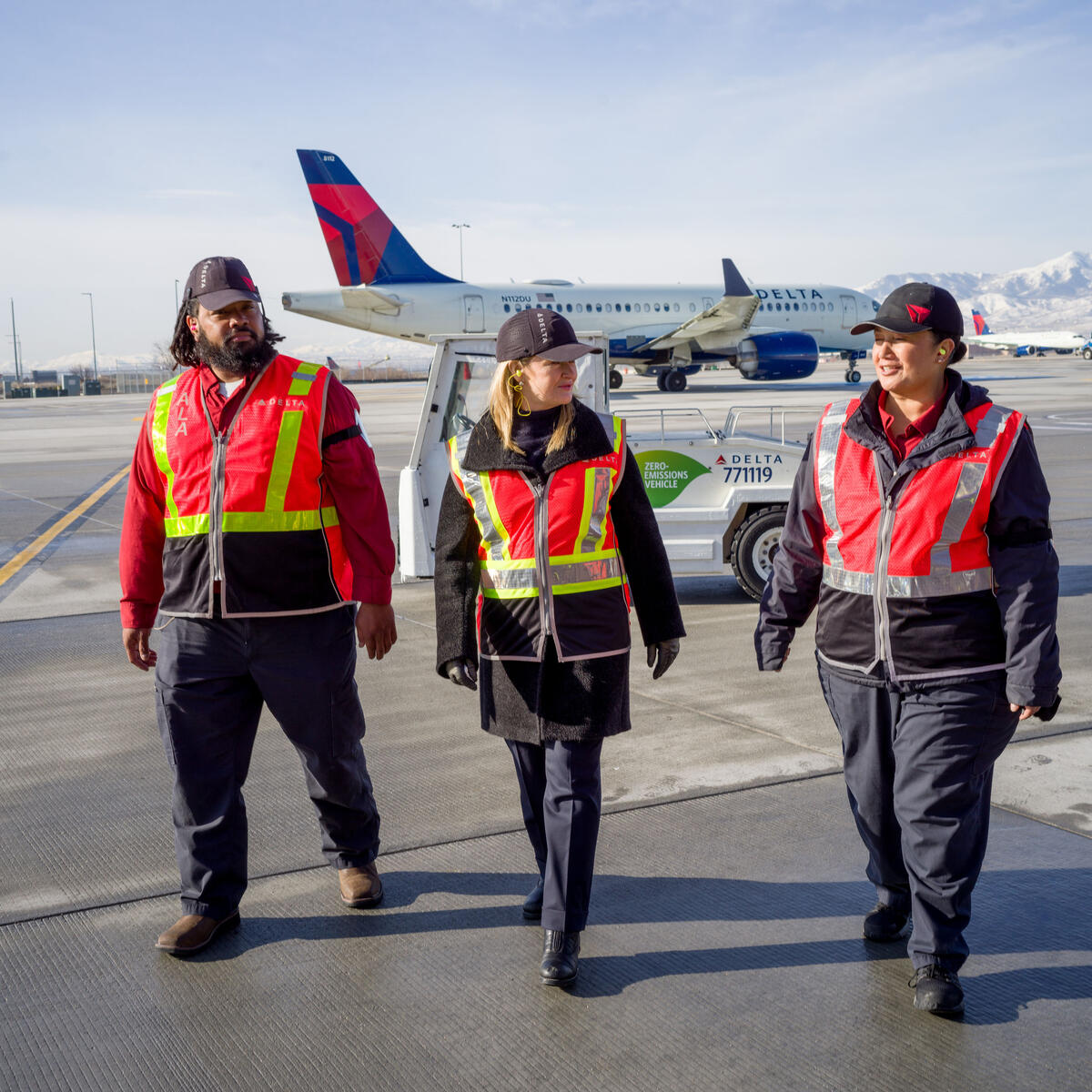 Delta Chief Sustainability Officer Pam Fletcher (middle) talks with Aircraft Load Agent Thomas Tuikolovatu (left) and Ramp Agent Sinai Pauni (right) about how they use eGSE at Salt Lake City International Airport (SLC).
