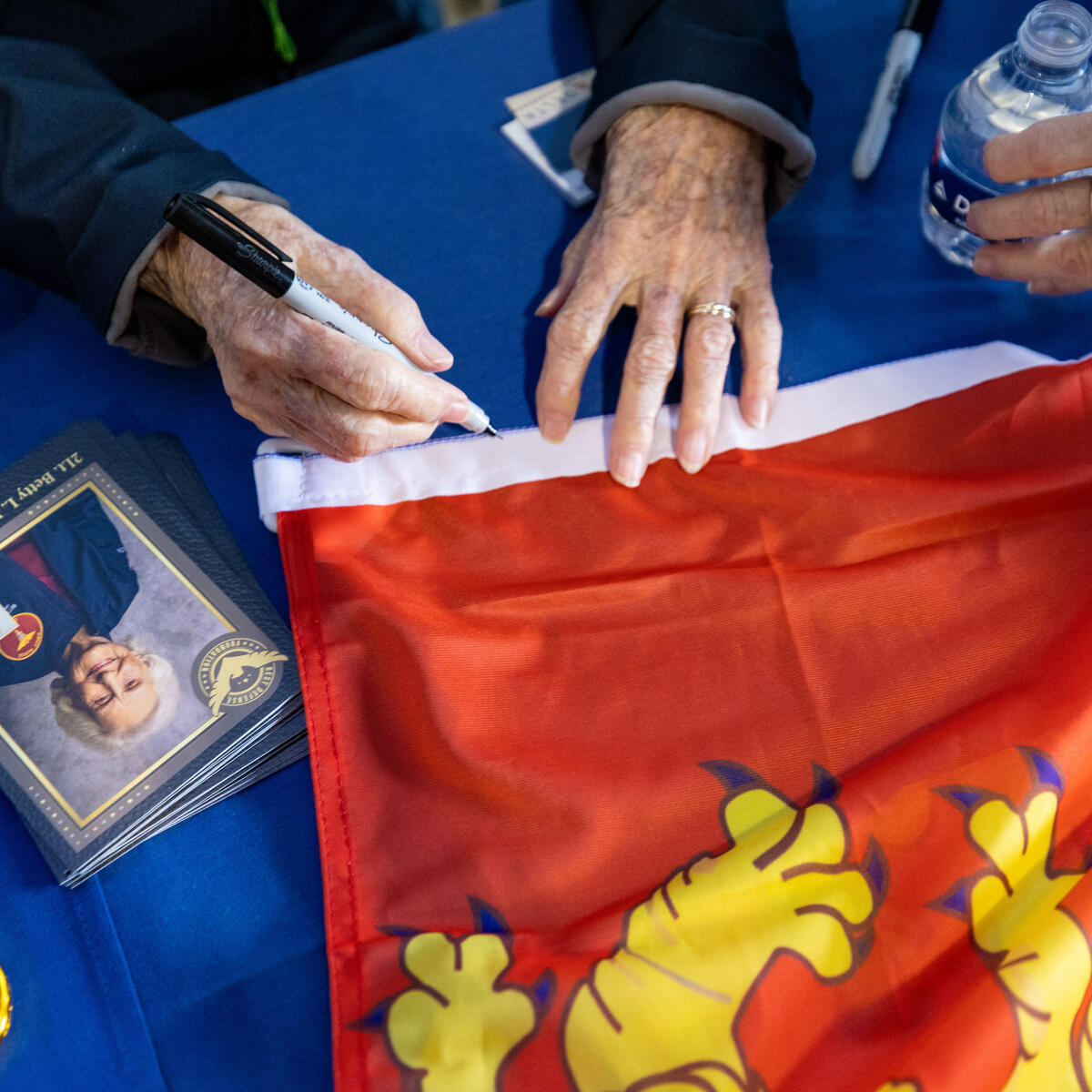 2Lt. Betty Rosevear signs memorabilia during a lunch that preceded the sendoff of more than 40 WWII veterans to Normandy, France, for the 79th annual commemoration of the 1944 D-Day invasion. 