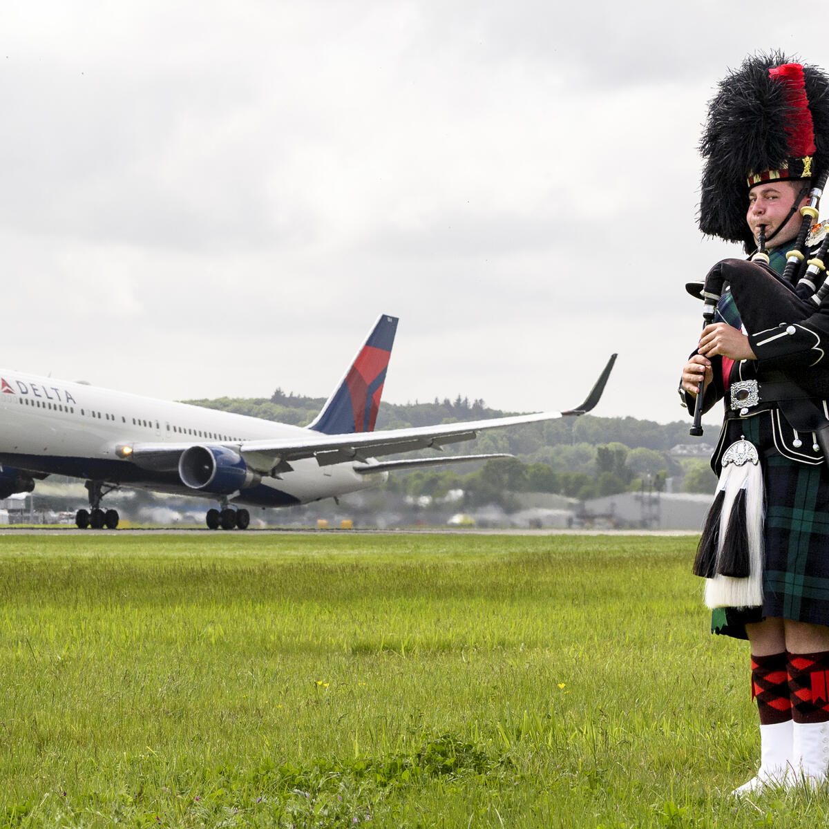 A bagpiper plays in front of a Delta aircraft at the Edinburgh Airport.