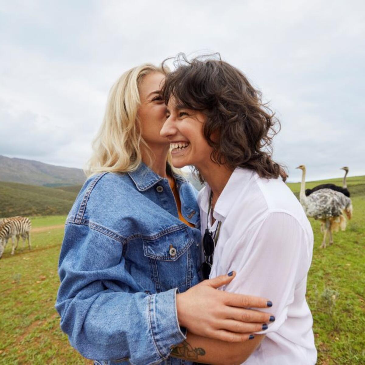 Two women smiling with ostriches and zebras behind them