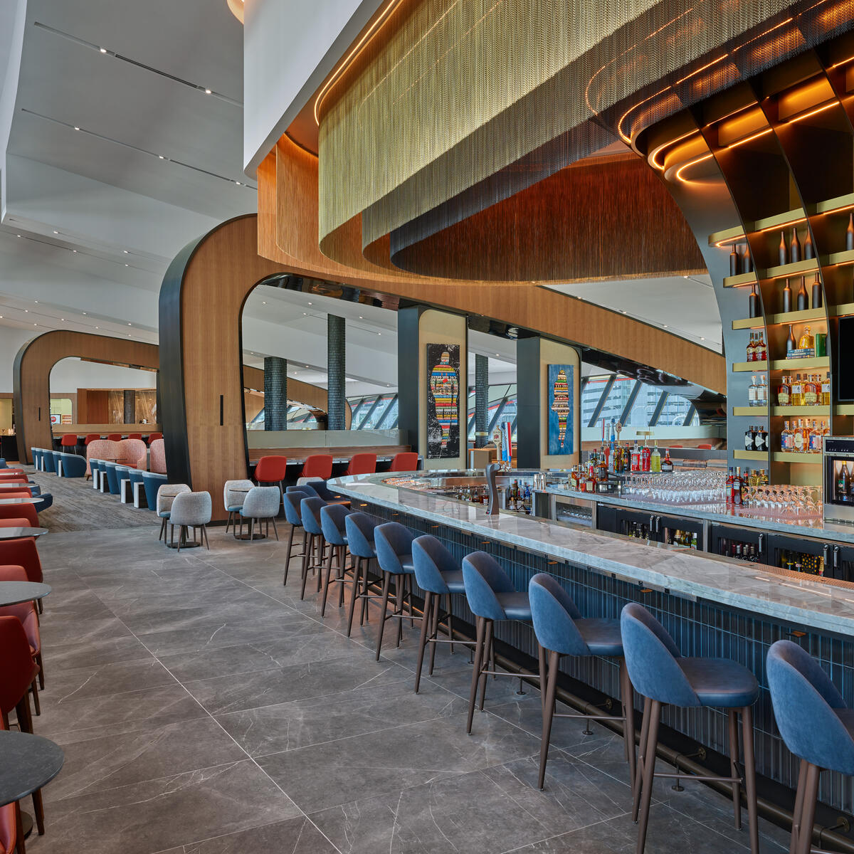 Perhaps the most eye-catching element of Delta's newest Sky Club at Boston-Logan Airport is the premium bar, which features a layered, champagne-toned mesh ceiling overhang and a dramatic backlit beverage display. 