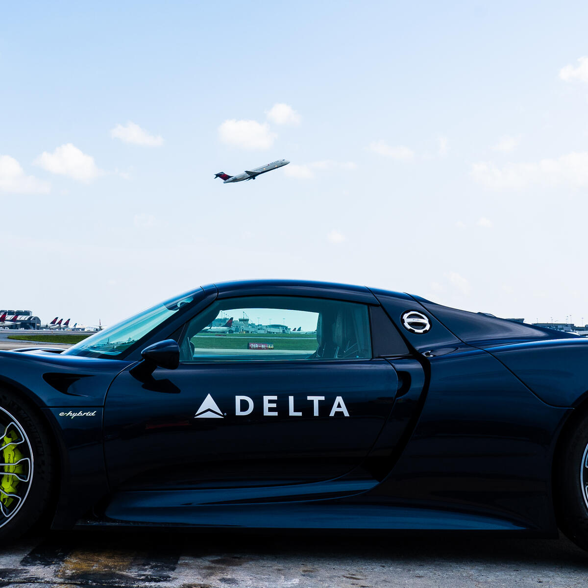 A Delta Boeing 717 takes off above a Porsche 918 Spyder at Hartsfield-Jackson Atlanta International Airport.