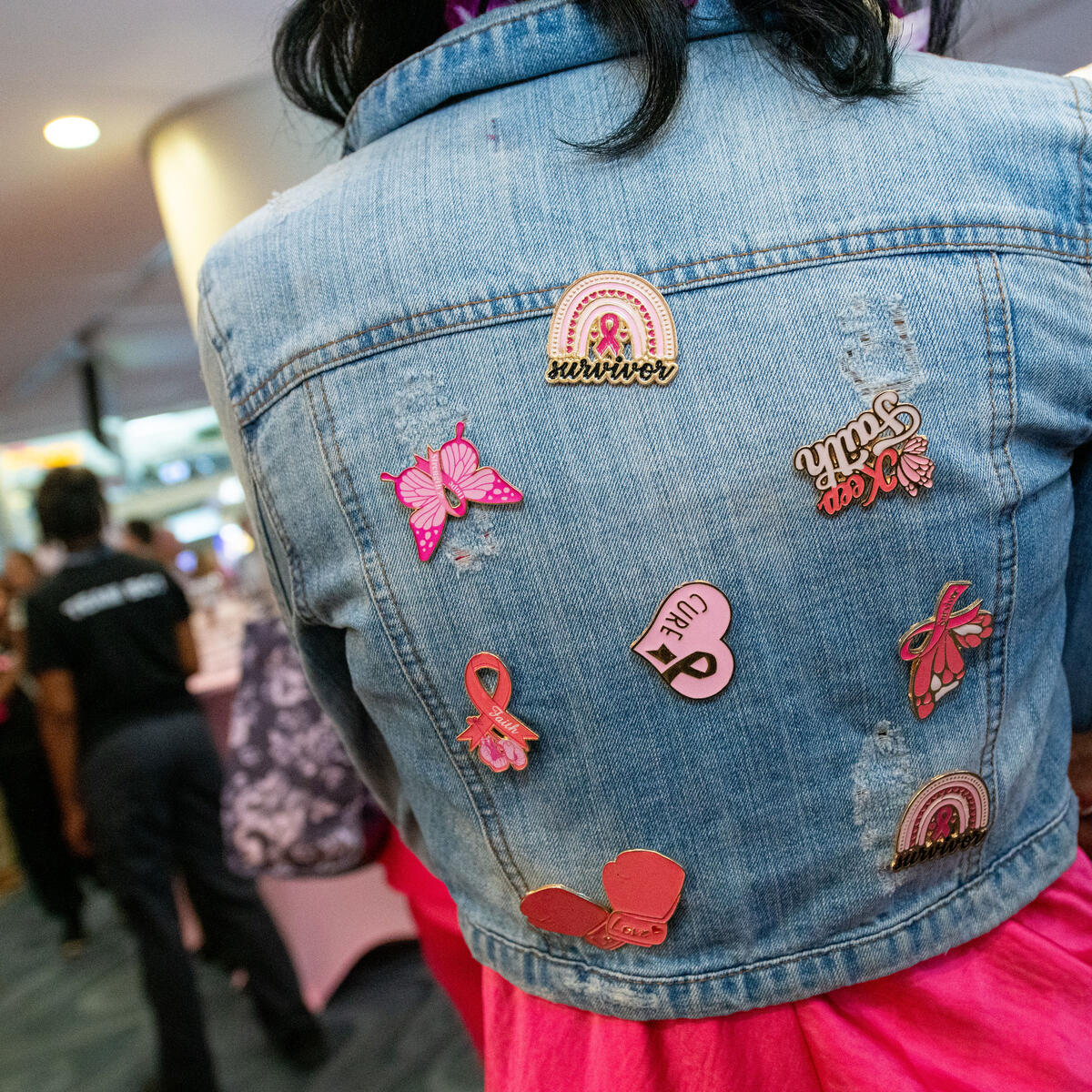A breast cancer survivor shows off her collection of Breast Cancer Awareness pins on the back of her jean jacket.